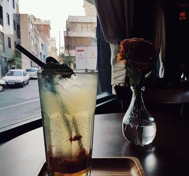 نوشیدنی خنک و گوارا در کافه پاییزا با تزئین برگ و گلدان گل روی میز، در کنار منظره زیبای خیابان از پنجره. فضایی دلنشین و آرام.