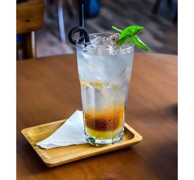 نوشیدنی خنک و تازه کافه پاییزا: کوکتل یا موهیتو با یخ، برگ‌های سبز معطر و نی فانتزی در لیوان بلند روی میز چوبی برای روزهای گرم.