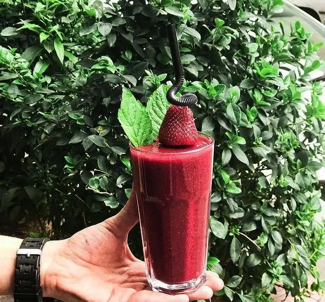 یک لیوان اسموتی توت فرنگی تازه و خوشرنگ کافه پاییزا، با تزئین برگ نعناع و توت فرنگی، نوشیدنی خنک و طبیعی برای روزهای گرم.