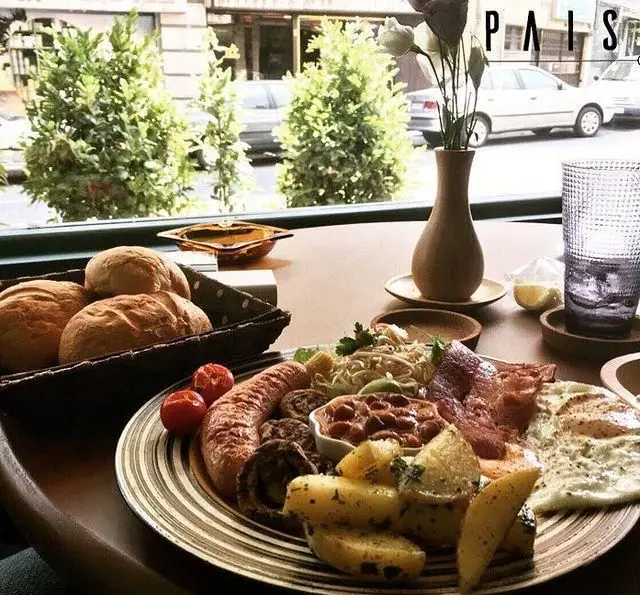 صبحانه کامل و لذیذ کافه پاییزا: سوسیس، بیکن، تخم‌مرغ، لوبیا، سیب‌زمینی، نان تازه و پاستا در فضایی دلپذیر با ویوی خیابان.