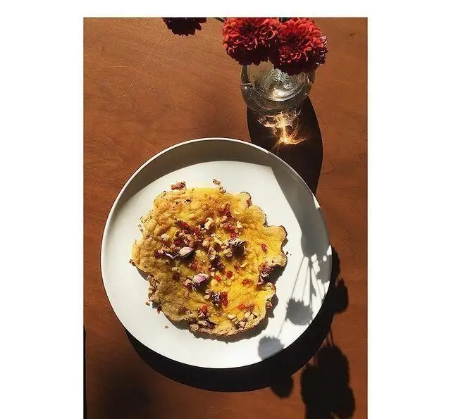 عکس جذاب صبحانه کافه پاییزا: املت زعفرانی با تزئین زرشک، گردو و گل محمدی، کنار گلدان گل قرمز در فضایی دنج و آفتابی.