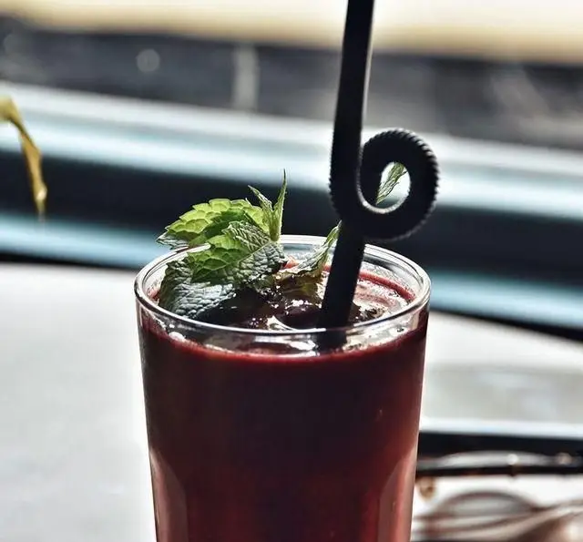 اسموتی قرمز رنگ و با طراوت با برگ‌های نعنای تازه و نی پیچ‌دار در کافه پاییزا، انتخابی سالم و خوش‌طعم برای مشتریان.