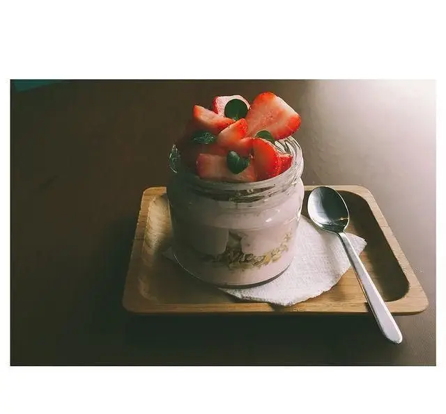 پارافه توت فرنگی و گرانولا با ماست میوه ای تازه، آماده برای سرو در فضای دنج و زیبای کافه پاییزا.