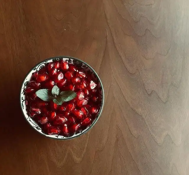 کاسه‌ای زیبا از دانه انار شیرین و تازه با برگ‌های معطر نعناع روی میز چوبی کافه پاییزا. انتخابی عالی برای تجربه‌ای دلپذیر.