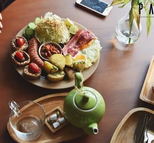 بشقاب صبحانه انگلیسی کامل و جذاب کافه پاییزا شامل تخم مرغ، بیکن، سوسیس، لوبیا، سیب زمینی، قارچ و سالاد. نوشیدنی چای در فضای دلنشین.