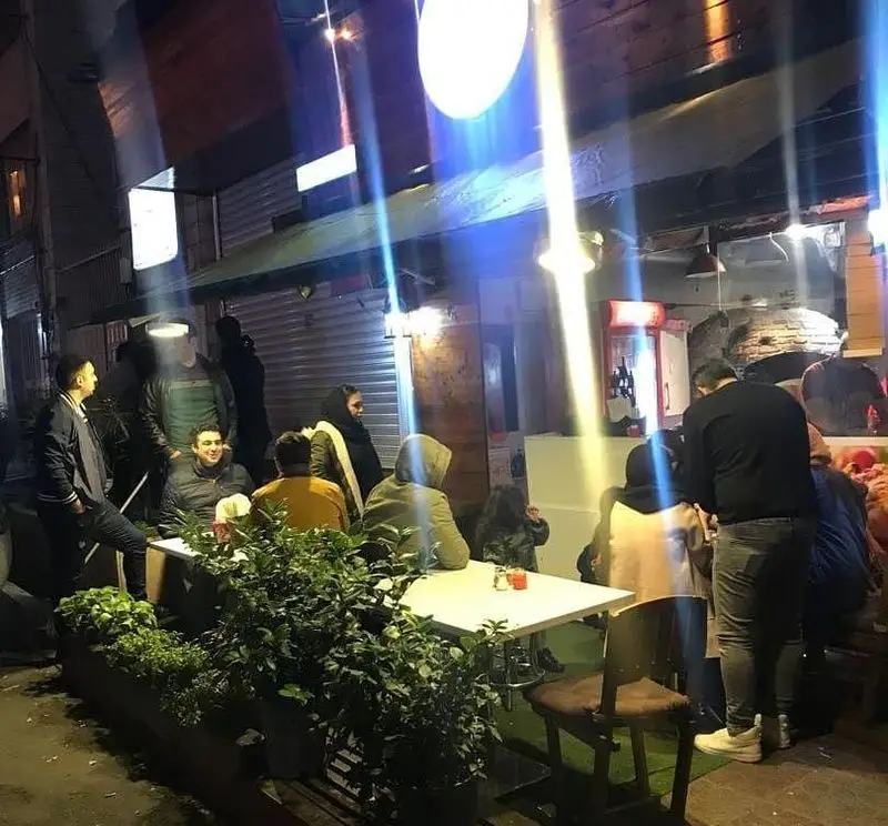 نمایی شبانه از پیتزا پیلا لویزان با مشتریان نشسته در فضای باز، محیطی گرم و دلنشین برای صرف پیتزا در تهران.