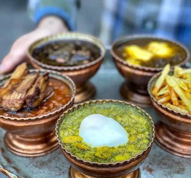 سفره‌ای رنگارنگ از اصیل‌ترین خورش‌های ایرانی و گیلانی رستوران گیلار در ظروف مسی زیبا؛ باقالی قاتوق، قیمه، قورمه سبزی و سیب‌زمینی سرخ کرده.