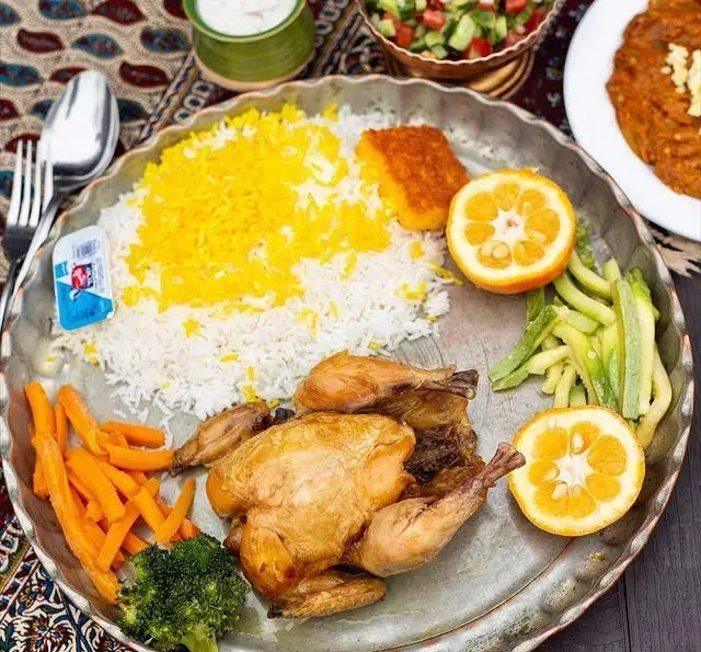 تصویری از غذای لذیذ رستوران گیلار: پلو مرغ با مرغ بریان آبدار، برنج زعفرانی معطر، سبزیجات تازه، ته دیگ و نارنج. یک وعده کامل ایرانی.