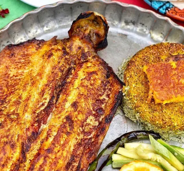 ماهی کبابی طلایی رستوران گیلار با سبزی پلو زعفرانی و ته دیگ خوشرنگ در یک سینی فلزی. یک غذای گیلانی اصیل و لذیذ.