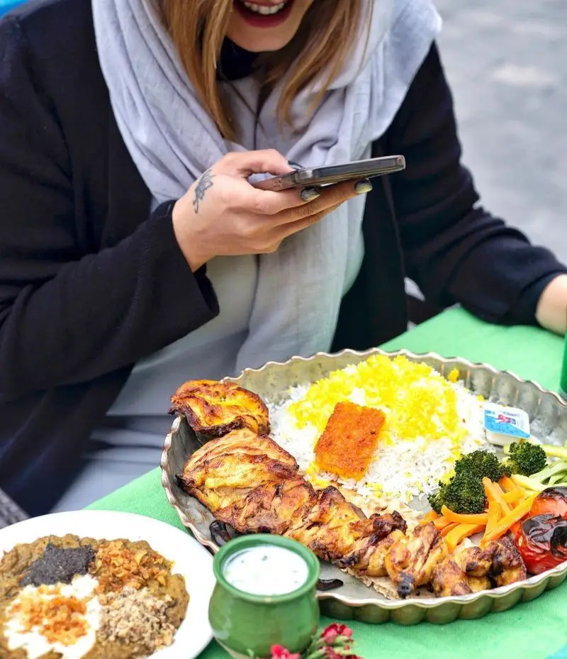مشتری در رستوران گیلار از سینی باشکوه انواع کباب، برنج زعفرانی و کشک بادمجان با موبایل عکس می‌گیرد. غذای اصیل ایرانی.