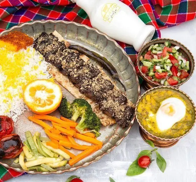 یک سینی پر از غذای لذیذ ایرانی رستوران گیلار: کباب، پلو زعفرانی، باقالی قاتوق، سالاد شیرازی، سبزیجات تازه و دوغ.