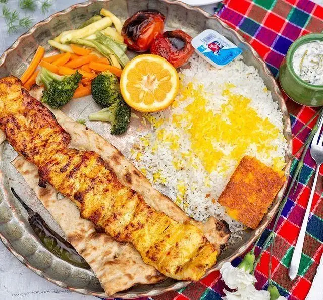 یک بشقاب غذای لذیذ رستوران گیلار شامل کباب جوجه آبدار روی نان، پلو زعفرانی، گوجه کبابی، سبزیجات تازه و ماست. غذای اصیل ایرانی.