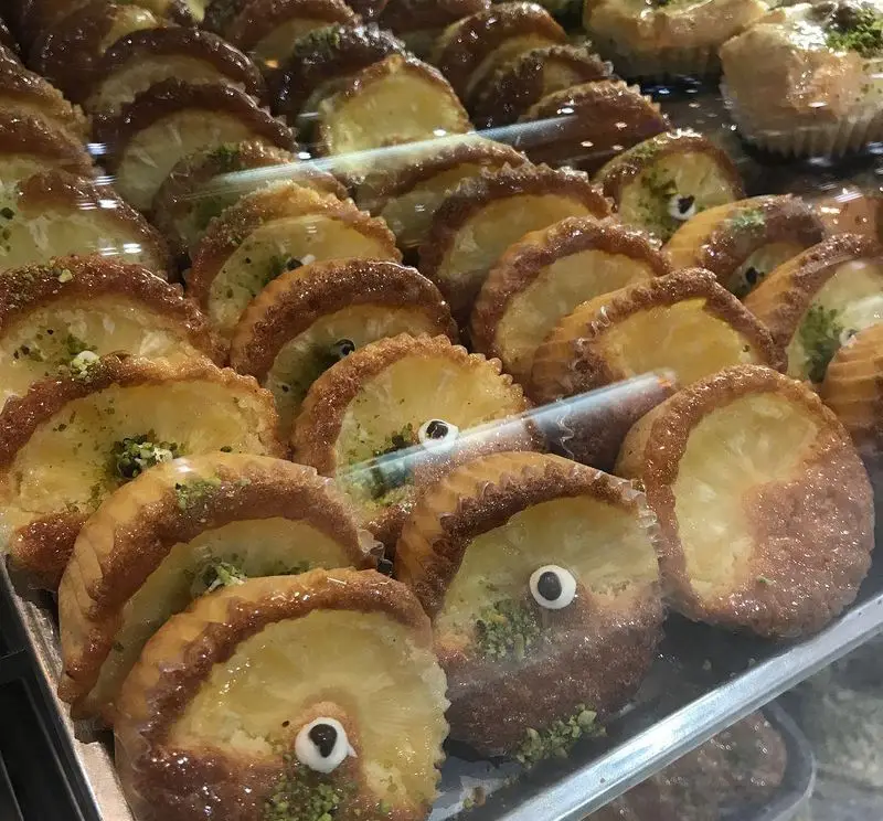 شیرینی های متنوع و خوشمزه کافه قنادی لادن شامل دسرهای آناناسی با تزیین پسته و طرح های خاص، آماده سرو در کافه.