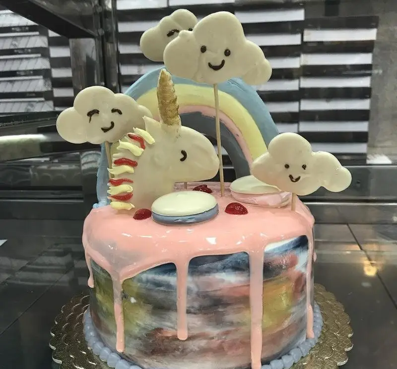 کیک تولد یونیکورن خاص با ابرهای بامزه و رنگین‌کمان، طراحی هنرمندانه و خوشمزه از کافه قنادی لادن برای لحظات شیرین شما.