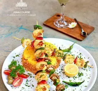 کافه چراغان بام لند: غذای اصلی میگو اسپایسی خوشمزه و سیخ‌های میگو تازه با برنج و سبزیجات در رستوران کافه چراغان بام لند.