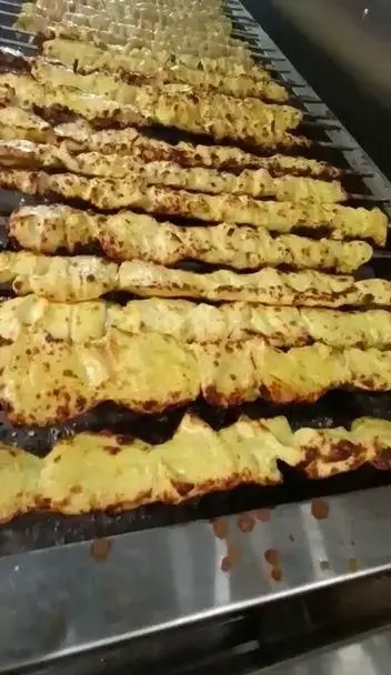 ردیف‌های کباب مرغ زعفرانی تهران کباب در حال پخت روی گریل داغ. تجربه طعم بی‌نظیر جوجه کباب با کیفیت بالا.