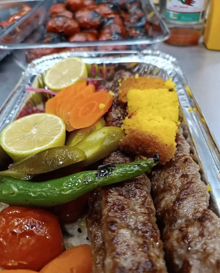 کباب کوبیده مخصوص تهران کباب، یک غذای سنتی و لذیذ ایرانی با دورچین تازه از لیمو، ترشیجات و گوجه فرنگی کبابی، آماده سرو.