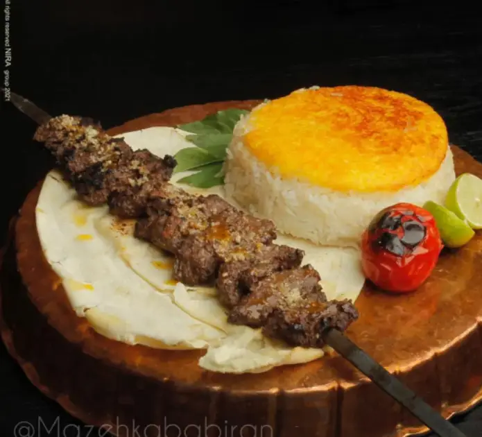 کباب گوشت لذیذ رستوران مزه کباب گیشا همراه با برنج ته دیگ زعفرانی، نان تازه، گوجه کبابی و لیمو، غذایی اصیل و دلچسب.