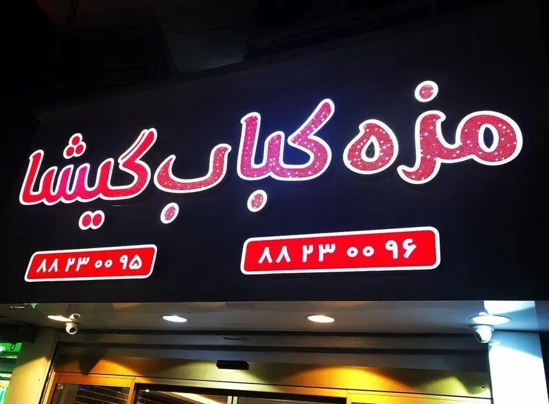 تابلوی روشن و درخشان رستوران مزه کباب گیشا در شب با متن قرمز رنگ و شماره تماس‌های ۸۸۲۳۰۰۹۵ و ۸۸۲۳۰۰۹۶ برای سفارش غذا.