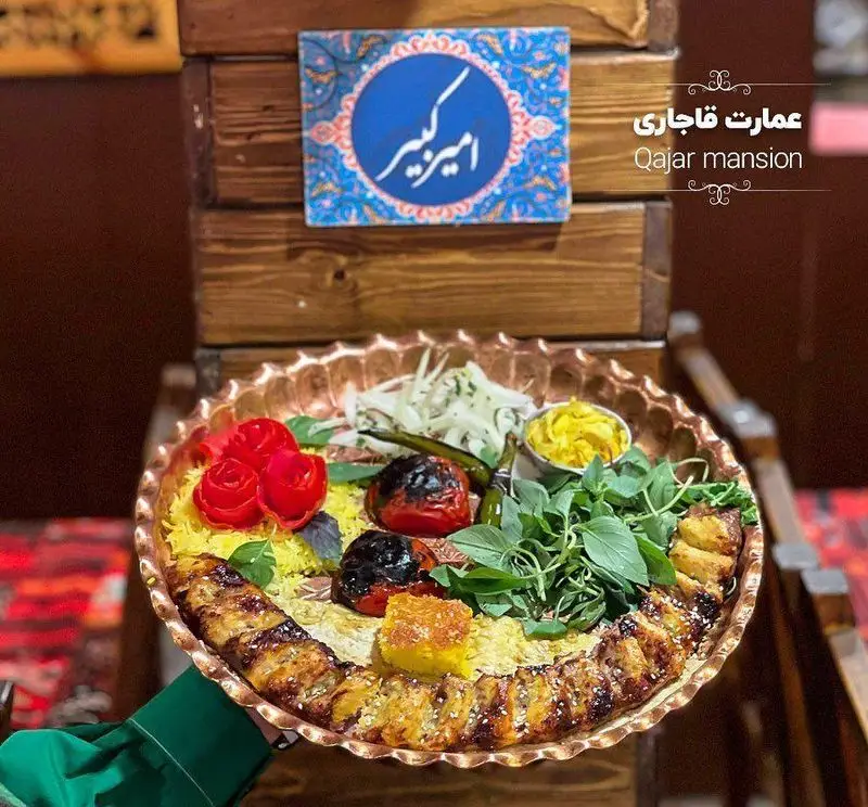 عکس یک سینی مسی بزرگ پر از کباب و برنج زعفرانی، گوجه کبابی و سبزی تازه در رستوران سنتی عمارت قاجاریه.