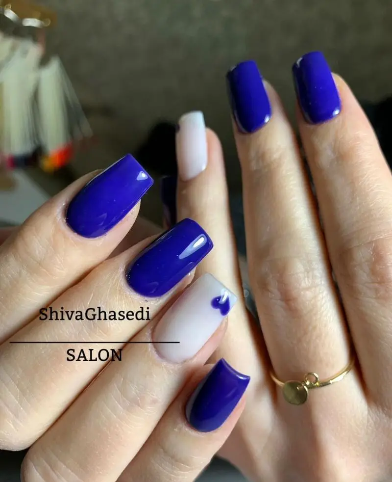 طراحی ناخن دخترانه شیک با لاک آبی کاربنی تیره و ناخن سفید با طرح قلب آبی کوچک به همراه انگشتر طلا در سالن شیوا قاصدی