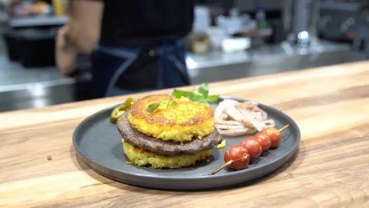 تصویری از برگر منحصر به فرد اینجا برگر؛ پتی‌های گوشت بین دو لایه برنج زعفرانی ته دیگی، با دورچین تازه.