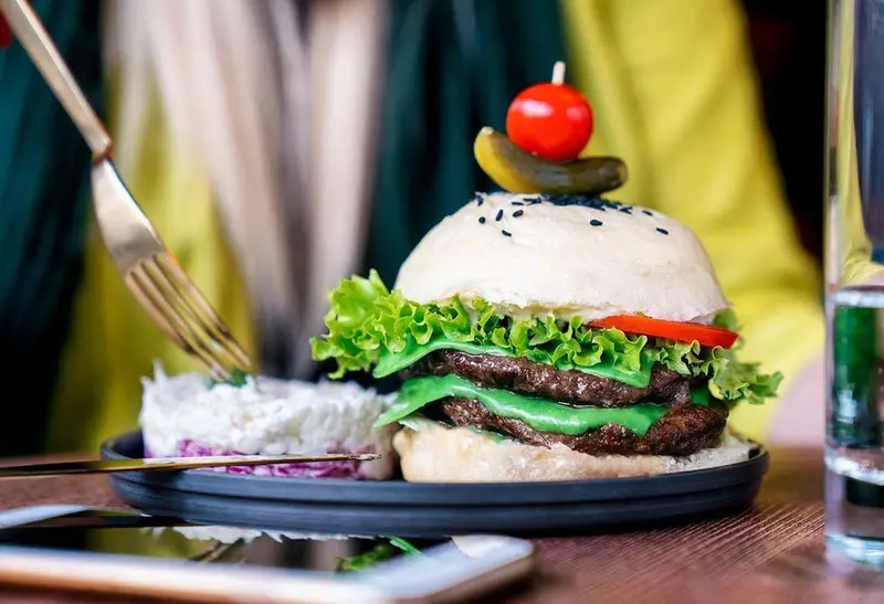 یک برگر دو طبقه خوشمزه اینجا برگر با پنیر سبز، کاهو، گوجه، نان کنجدی، گوجه گیلاسی و خیارشور، همراه سالاد.