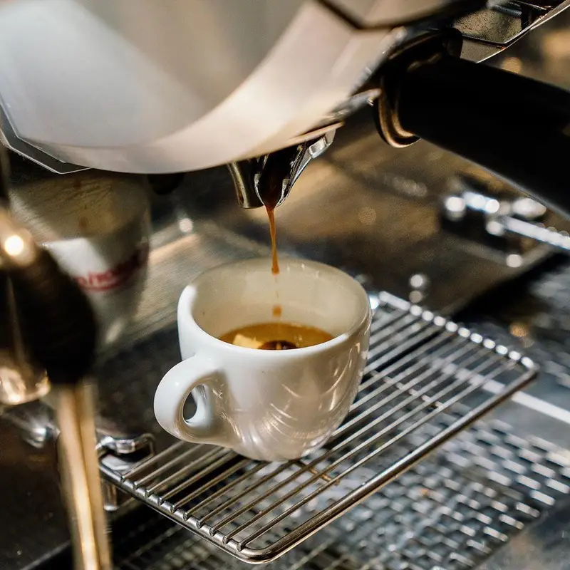 تصویری جذاب از دستگاه اسپرسو در حال ریختن قهوه تازه در فنجان سفید، ارائه دهنده نوشیدنی‌های باکیفیت در اینجا برگر.