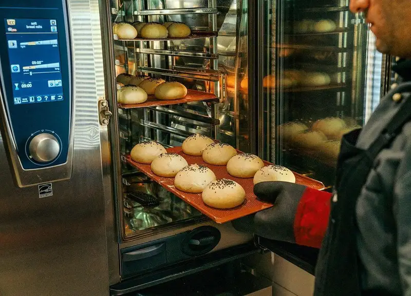 پخت نان همبرگر تازه و باکیفیت در فر صنعتی پیشرفته اینجا برگر با کنجد، تضمین طعم و عطر بی‌نظیر برای ساندویچ‌های ما.