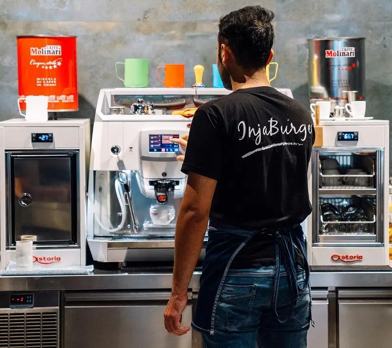 باریستای اینجا برگر در حال آماده‌سازی قهوه با دستگاه اسپرسوساز پیشرفته Molinari. تجربه نوشیدنی قهوه تازه در کافه اینجا برگر.