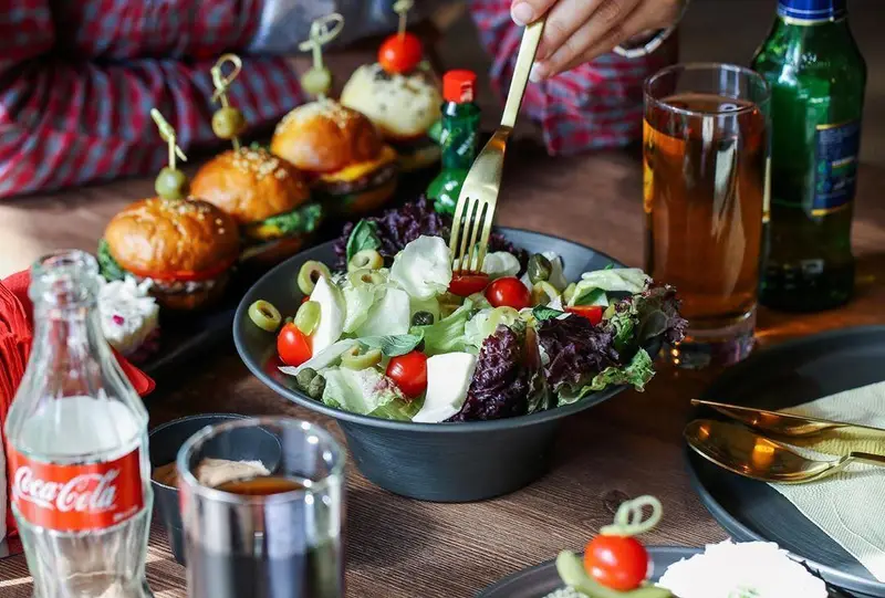 مشتری در اینجا برگر مشغول لذت بردن از سالاد تازه و نوشیدنی است. مینی برگرهای خوشمزه اینجا برگر نیز در پس زمینه دیده میشوند.