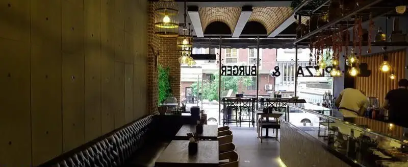 نمای داخلی دنج و شیک رستوران برگر تهران برگر با طراحی مدرن، نورپردازی خاص، میز و صندلی‌های چوبی و فضای دلنشین برای مشتریان.