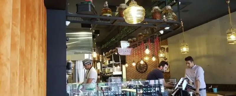 فضای داخلی کافه/رستوران برگر تهران برگر با کارکنان مشغول خدمات‌دهی، دکوراسیون صنعتی، نورپردازی دلنشین و قفسه‌های تزئینی جذاب.