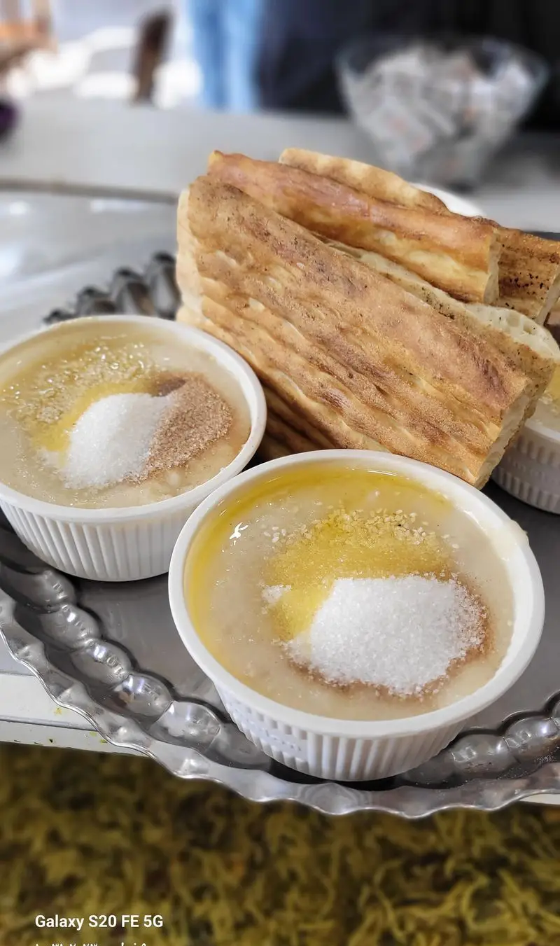 حلیم سنتی و خوشمزه آش و حلیم حاج مهدی با کره محلی، شکر و پودر دارچین در کاسه، کنار نان تازه تافتون بر سینی.