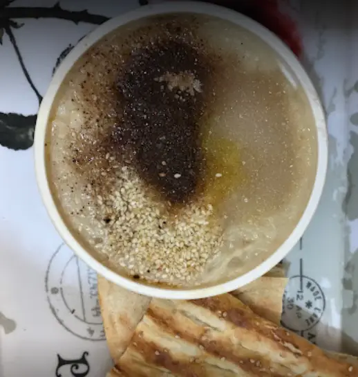 کاسه‌ای حلیم یا آش داغ و خوشمزه از آش و حلیم حاج مهدی با کنجد، ادویه و روغن. کنار آن نان تازه برای یک صبحانه سنتی و اصیل ایرانی.