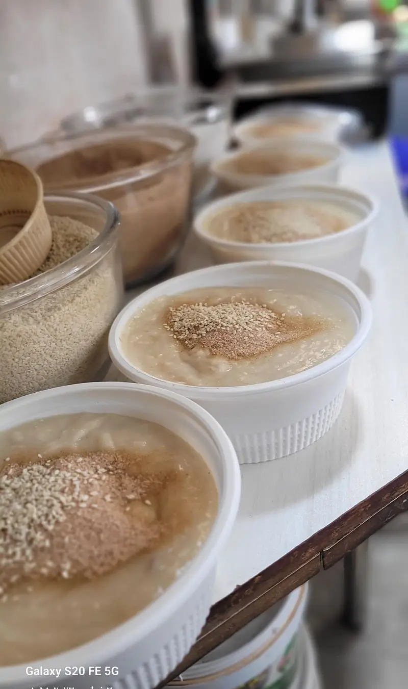 کاسه‌های حلیم تازه و خوش‌طعم حاج مهدی، با تزئین کنجد و ادویه‌جات معطر، آماده سرو. مواد اولیه آش و حلیم نیز در پس‌زمینه.