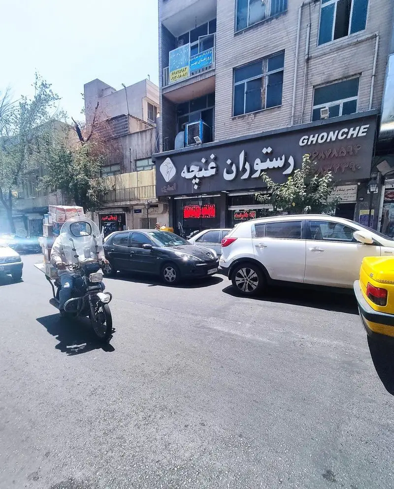 نمایی از رستوران غنچه در تهران، با تابلوی کسب و کار "GHONCHE"، خیابانی پر از ماشین و موتورسوار در یک روز آفتابی.