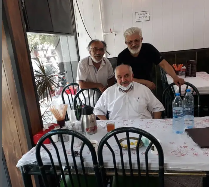 تصویری از مشتریان خوشحال رستوران غنچه. سه مرد مسن با لبخند در محیطی دلنشین دور یک میز نشسته و ایستاده‌اند، آماده سرو غذا.