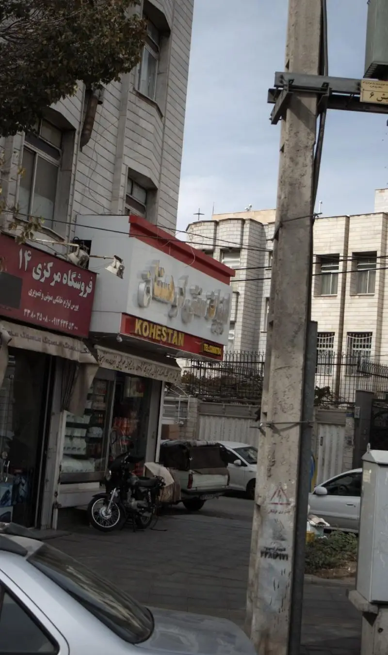 ورودی فروشگاه لبنیات سنتی کوهستان در یک خیابان شهری شلوغ، با تابلوی برجسته KOHESTAN و نمایی از ساختمان‌های اطراف.