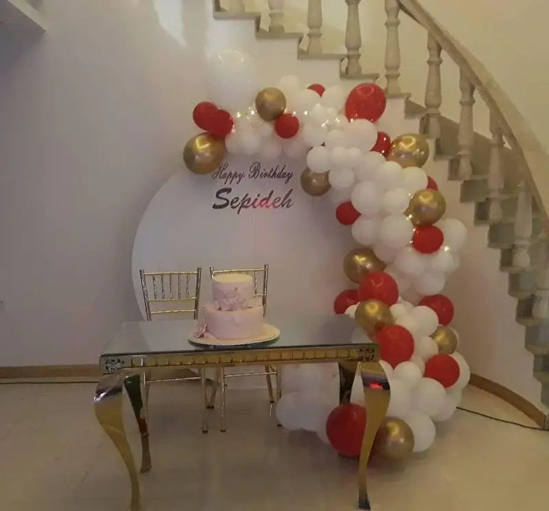 نمونه بادکنک‌آرایی و دکور شیک تولد با تم قرمز و طلایی، میز شیشه‌ای و صندلی اجاره‌ای، ارائه شده توسط تجهیزات و ظروف کرایه ستاره.