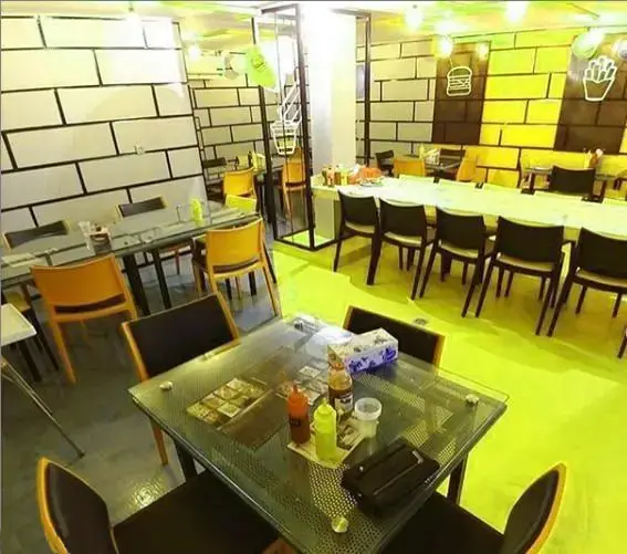 فضای داخلی جذاب فست فود بشکه با دکوراسیون مدرن، دیوار آجری سیاه و زرد و سفید، میزهای شیشه‌ای و صندلی‌های شیک و راحت برای مشتریان.