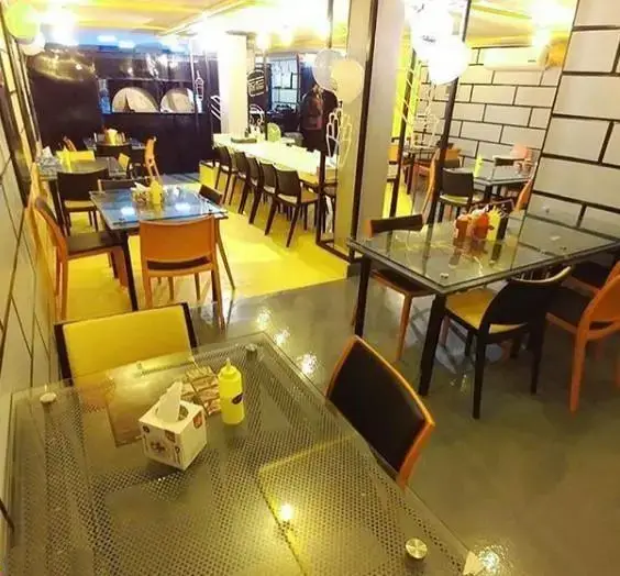 دکوراسیون داخلی فست فود بشکه با میزهای شیشه‌ای، صندلی‌های مدرن و کفپوش زرد روشن، فضایی دعوت‌کننده و مناسب برای سرو غذای آماده.