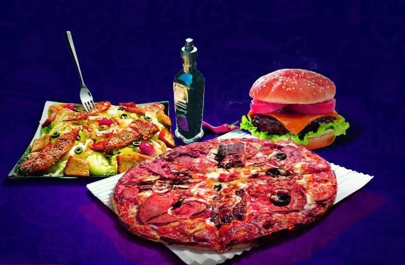 نمایی از میز غذای فست فود سیر و پیاز: پیتزای بزرگ، همبرگر آبدار، سالاد سزار با مرغ و بطری سس، ایده آل برای سفارش آنلاین.