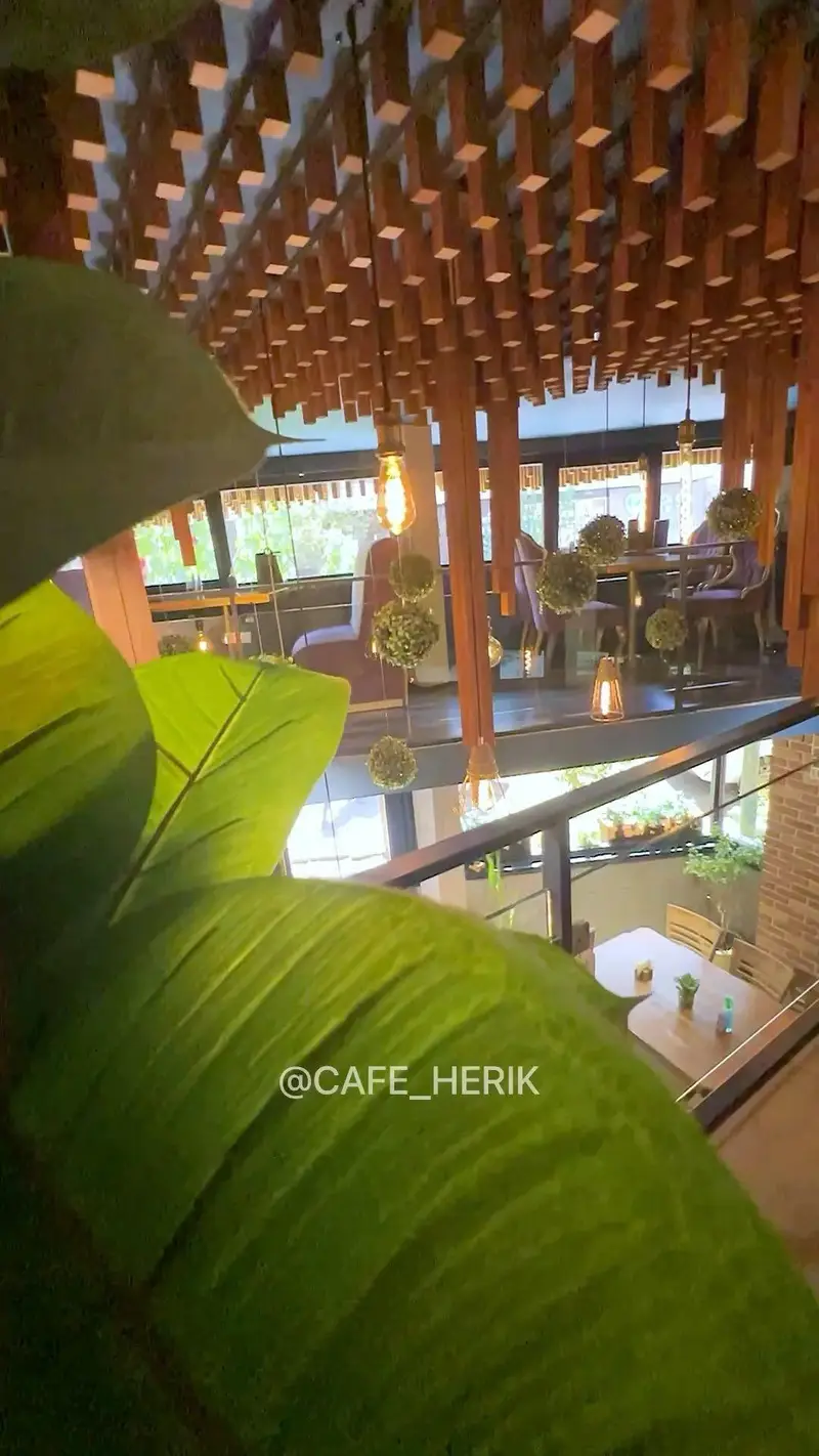 فضای داخلی دنج و مدرن کافه رستوران هریک با سقف چوبی شیک، گیاهان سبز تزئینی و نورپردازی گرم، محیطی آرام برای مشتریان.