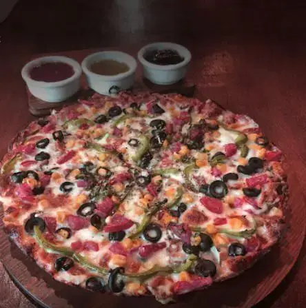 پیتزا مخصوص پرطرفدار کافه رستوران هریک با تاپینگ‌های رنگارنگ شامل زیتون، فلفل سبز، ذرت و کالباس، ایده‌آل برای یک وعده کامل.