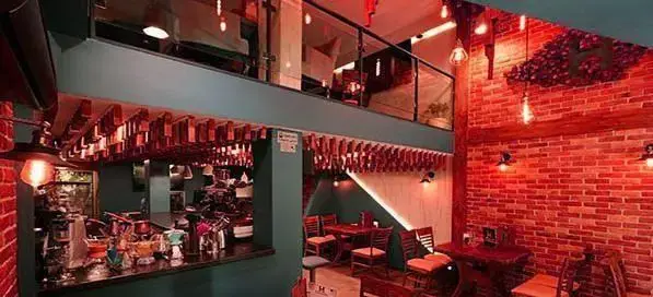 نمایی زیبا از کافه رستوران هریک، با طراحی داخلی مدرن و جذاب، فضای نشیمن، بار، بالکن، دیوارهای آجری و نورپردازی گرم.