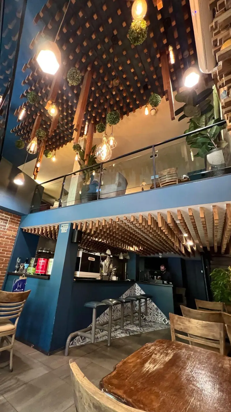 دکوراسیون داخلی مدرن و دنج کافه رستوران هریک با سقف چوبی جذاب، نورپردازی گرم، بار، میز و صندلی چوبی در دو طبقه.