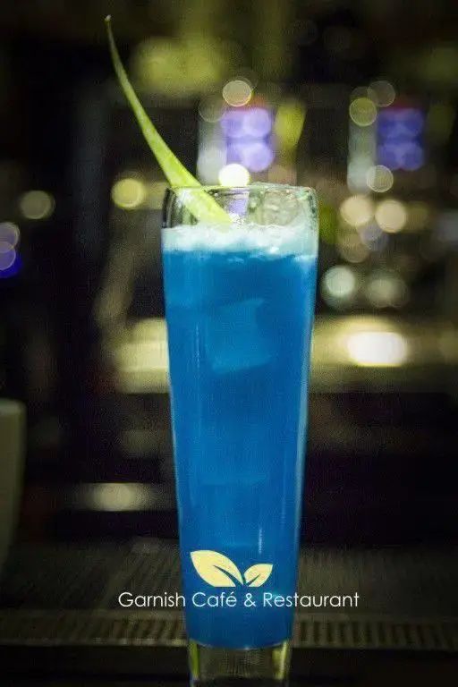 نوشیدنی کوکتل آبی با برگ سبز در لیوان بلند، جلوه‌ای خاص از منوی کافه رستوران گارنیش برای تجربه‌ای به یادماندنی.