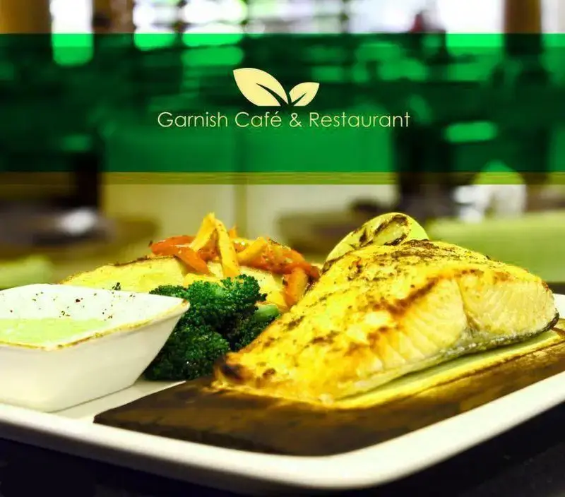 نمایی نزدیک از یک پرس غذای سالم و لذیذ، شامل ماهی گریل شده با سس مخصوص، بروکلی تازه و سبزیجات فصل در منوی کافه رستوران گارنیش.