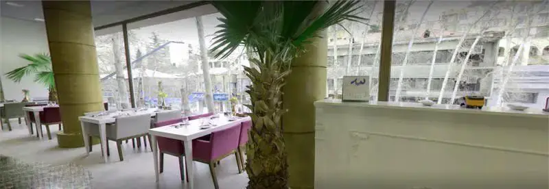فضای داخلی دنج و شیک کافه رستوران گارنیش با میز و صندلی‌های مدرن، پنجره‌های بزرگ و منظره درختان، مناسب برای دورهمی و قرارهای دوستانه